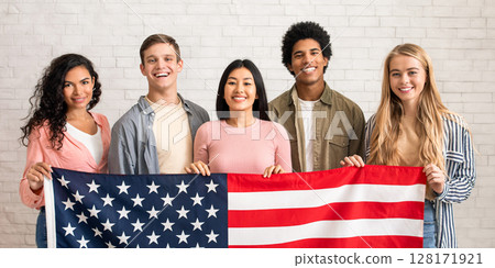 Immigration, relocation and study abroad. Cheerful young international students hold USA flag, looking at camera and ready to learn, on white brick wall background, copy space, studio shot 128171921