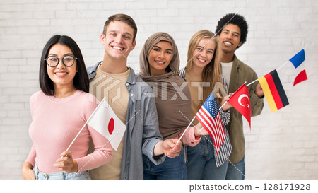 Exchange students and language school for different people. Funny digital young international pupils holding flags of USA, Japan, Turkey, Germany and France in classroom, studio shot, empty space 128171928