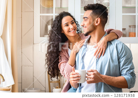 Happy Young Arab Spouses Hugging And Drinking Coffee In Cozy Kitchen Interior. Smiling Millennial Middle Eastern Couple Bonding At Home, Enjoying Spending Morning Time Together, Copy Space Happy Young Arab Spouses Hugging And Drinking Coffee In Cozy Kitchen Interior. Smiling Millennial Middle Eastern Couple Bonding At Home, Enjoying Spending Morning Time Together, Copy Space 128171938