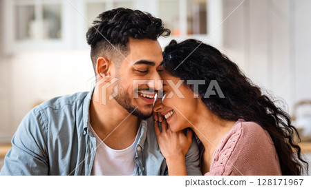 Happy Romantic Arab Couple Bonding While Having Breakfast In Kitchen, Cheerful Middle Eastern Newlyweds Enjoying Spending Time Together At Home, Embracing And Smiling While Eating Tasty Food, Closeup 128171967
