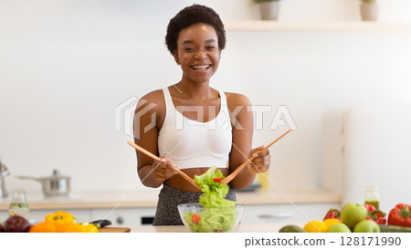 Happy African American Woman Cooking Healthy Food For Weight Loss Mixing Ingredients In Salad Bowl Standing In Modern Kitchen At Home, Smiling To Camera. Nutrition For Slimming And Dieting Happy African American Woman Cooking Healthy Food For Weight Loss Mixing Ingredients In Salad Bowl Standing In Modern Kitchen At Home, Smiling To Camera. Nutrition For Slimming And Dieting 128171990