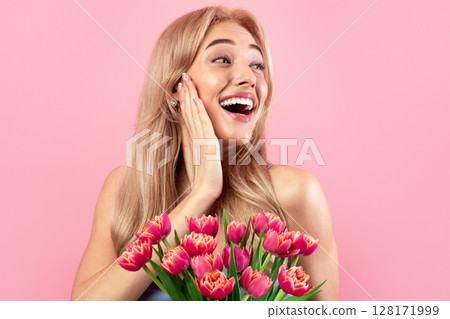 Portrait of beautiful young lady with lovely flowers feeling excited on pink studio background. Pretty blonde with bouquet of tulips as Woman's Day gift. Spring holiday concept 128171999