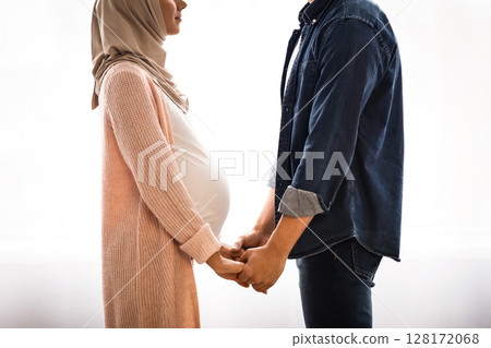 Side View Portrait Of Romantic Pregnant Muslim Couple Holding Hands At Home, Young Arabic Spouses Expecting For A Baby, Standing Together Near Window, Looking At Each Other With Love, Copy Space Side View Portrait Of Romantic Pregnant Muslim Couple Holding Hands At Home, Young Arabic Spouses Expecting For A Baby, Standing Together Near Window, Looking At Each Other With Love, Copy Space 128172068