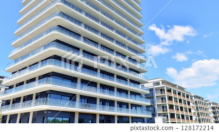 Exterior of a high modern multi-story apartment building - facade, windows and balconies. Modern glass balcony railings. Exterior of a high modern multi-story apartment building - facade, windows and balconies. Modern glass balcony railings. 128172214