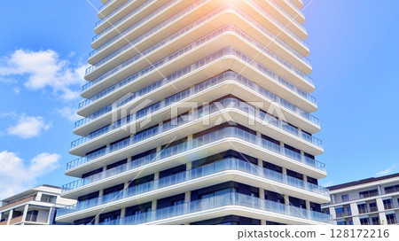 Exterior of a high modern multi-story apartment building - facade, windows and balconies. Modern glass balcony railings. Exterior of a high modern multi-story apartment building - facade, windows and balconies. Modern glass balcony railings. 128172216