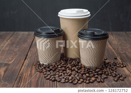 Mockup coffee in a disposable cup on a wooden table and coffee grains, dark background. Coffee background. Mockup coffee in a disposable cup on a wooden table and coffee grains, dark background. Coffee background. 128172752
