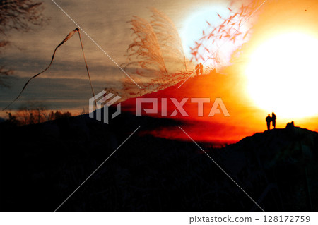 Silhouettes of couple standing on a hill with pampas grass and a large orange setting sun. Natural background filled with sunlight. Nature and people. 128172759