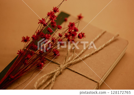 Kraft vintage natural simple brown cardboard notebook on brown table. Ecological ribboned paper diary and red small flowers bouquet. Summer memories. 128172765