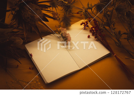 An open notebook on a table next to dried exotic flowers. Still life in dark key with a copybook on a brown background. Floral botanical plants. An open notebook on a table next to dried exotic flowers. Still life in dark key with a copybook on a brown background. Floral botanical plants. 128172767