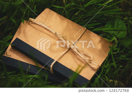 Kraft vintage natural simple brown cardboard notebooks lie on green grass top view. Goods for school and learning. Ecological ribboned paper diaries. 128172768