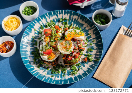 Soft boiled eggs served with toast and pesto with avocado and red onion, served on a beautiful blue and white plate. A breakfast set illuminated by the morning sun. 128172771
