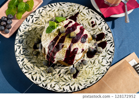 Fluffy matcha pancakes topped with juicy blueberries and velvety whipped cream, adorned with fresh mint leaves. Served on a white plate, glowing in morning sunlight   a vibrant, delicious breakfast  128172952