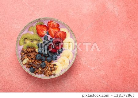 Delicious acai bowl with fresh fruits and granola in white ceramic bowl on pink table top view, healthy breakfast or snack, copy space 128172965