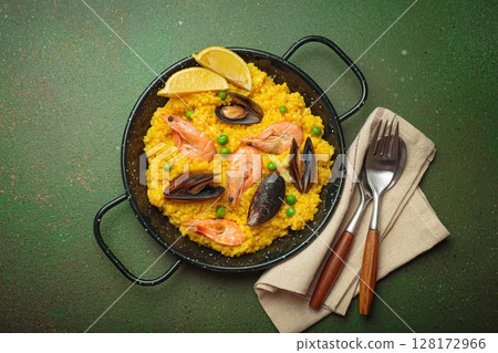 Spanish seafood Paella with shrimps, mussels, peas and lemon in a pan on green rustic background top view Spanish seafood Paella with shrimps, mussels, peas and lemon in a pan on green rustic background top view 128172966