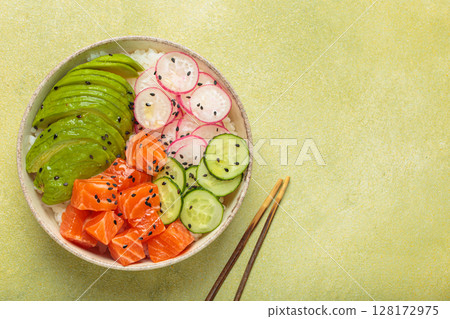 Salmon poke bowl with avocado, radish, cucumber and rice on green background top view, space for text Salmon poke bowl with avocado, radish, cucumber and rice on green background top view, space for text 128172975