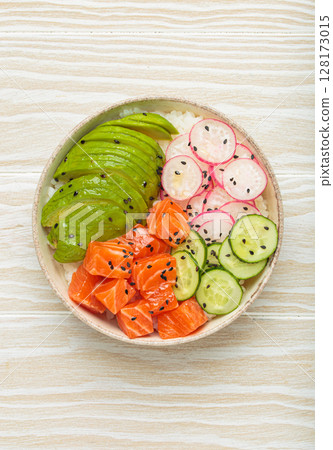 Salmon poke bowl with avocado, radish, cucumber and rice on white wooden background top view Salmon poke bowl with avocado, radish, cucumber and rice on white wooden background top view 128173015
