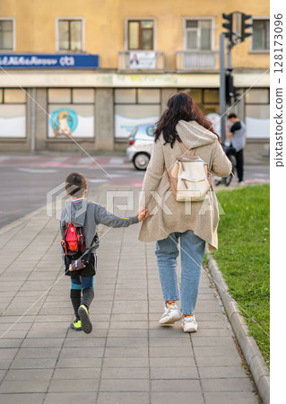 Anonymous woman and child walking hand in hand on city sidewalk after sport school. Concept of motherhood, sport, urban routine, family bonding, family connection 128173096