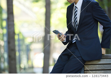 A young businessman in a suit looking at a smartphone in a business district 128173443