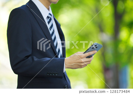 A young businessman in a suit looking at a smartphone in a business district A young businessman in a suit looking at a smartphone in a business district 128173484