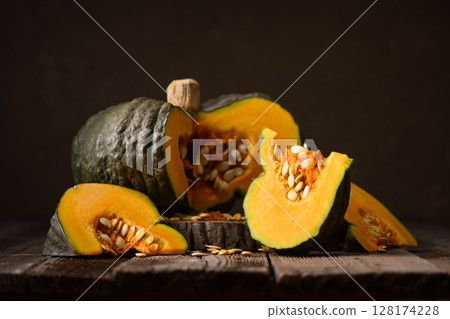 Green pumpkin cut open to reveal orange inside on rustic board 128174228