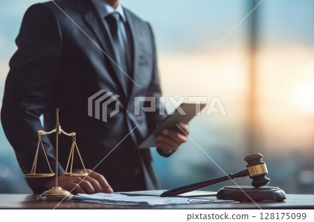 A man in a suit stands in front of a scale and a gavel 128175099