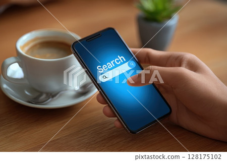 Closeup of male hands interacting with smartphone screen while holding coffee cup on a wooden table Closeup of male hands interacting with smartphone screen while holding coffee cup on a wooden table 128175102