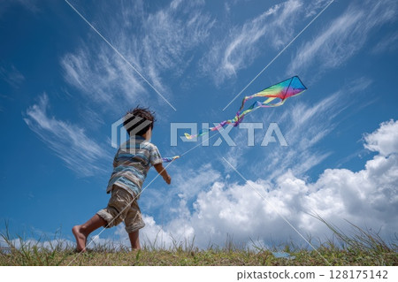 Child Flying a Colorful Kite on a Grassy Hill with Back Turned Against Bright Sky 128175142