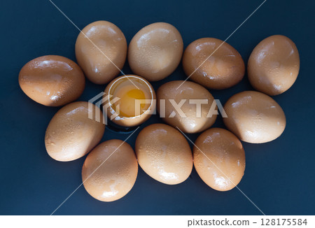 View of Egg yolk in Broken raw chicken eggshell in the among of Fresh chicken egg (Hen egg) on dark background. View of Egg yolk in Broken raw chicken eggshell in the among of Fresh chicken egg (Hen egg) on dark background. 128175584