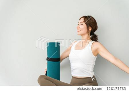 A woman wearing yoga wear/sportswear and a yoga mat 128175783