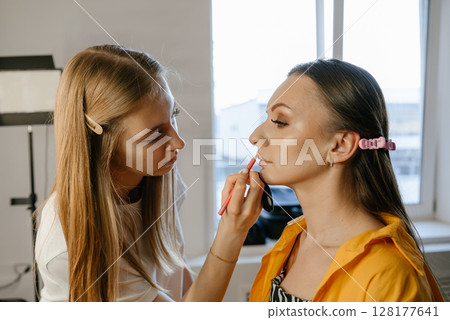 Makeup Artist Applying Lipstick to Model in Studio 128177641