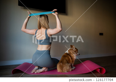 A young athletic woman does yoga with her dog at home. 128177704