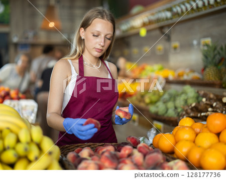 Girl shop seller add flat peach goods on display case in vegetable store 128177736