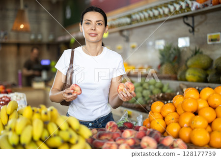 Focused woman shopping in organic food store, choosing flat peaches 128177739