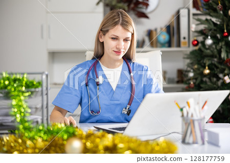 Physician woman sitting at table and using laptop during Christmastime 128177759