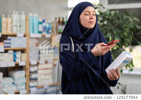 Young woman in hijab scanning qr code of cream 128177843