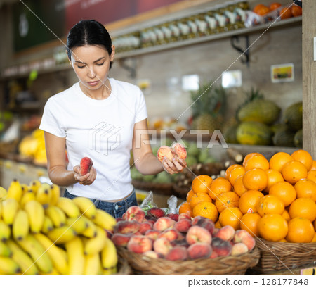 Focused woman shopping in organic food store, choosing flat peaches 128177848