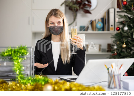 Portrait of business woman in protective mask with New Years tinsel and Christmas tree in office 128177850