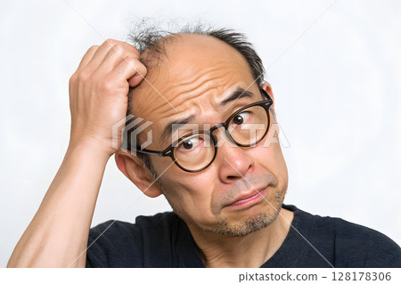 Close-up of a middle-aged man's troubled expression as he worries about his thinning hair Close-up of a middle-aged man's troubled expression as he worries about his thinning hair 128178306