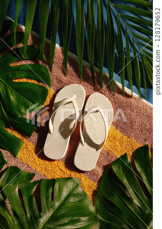 Pair of White Flip Flops on Colorful Beach Towel with Tropical Leaves in Sunlight Pair of White Flip Flops on Colorful Beach Towel with Tropical Leaves in Sunlight 128179652