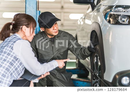 一名男汽車修理工和一名身著辦公室服裝的女前台工作人員在一輛車前交談 一名男汽車修理工和一名身著辦公室服裝的女前台工作人員在一輛車前交談 128179684