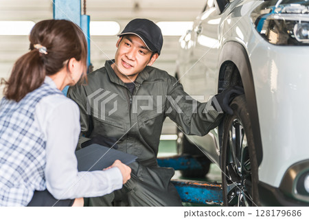 一名男汽車修理工和一名身著辦公室服裝的女前台工作人員在一輛車前交談 128179686