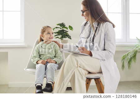 Little girl sitting with smiling doctor during hospital checkup while pediatrician cheering her up. Little girl sitting with smiling doctor during hospital checkup while pediatrician cheering her up. 128180146