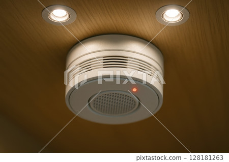 Close up of a modern white smoke detector with a red indicator light on a wooden ceiling Close up of a modern white smoke detector with a red indicator light on a wooden ceiling 128181263