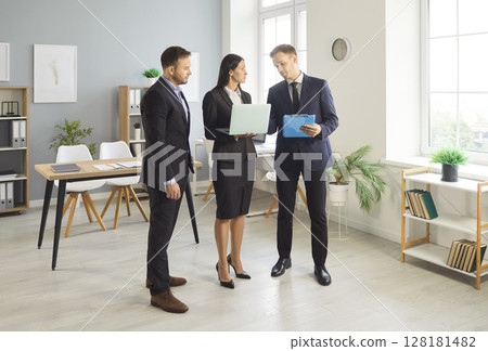Young business people standing with colleagues holding laptop on workplace in office 128181482