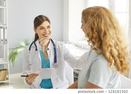 Female doctor with happy, friendly smile puts hand on shoulder of young woman to support her 128181502