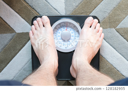 Legs of men standing on scales weight background fitness room. Concept of healthy lifestyle and sport Legs of men standing on scales weight background fitness room. Concept of healthy lifestyle and sport 128182935