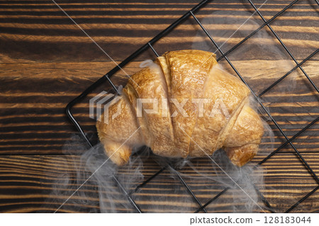 Freshly baked croissant on a cooling tray with a wooden background. Top view 128183044