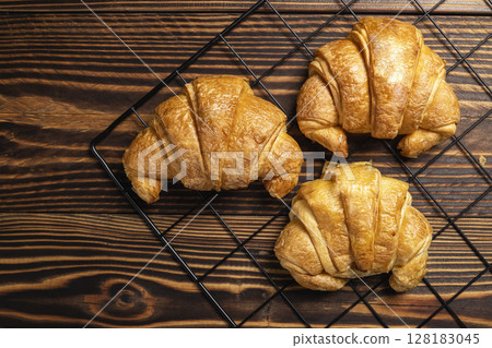 Freshly baked croissants on a cooling tray with a wooden background. Top view Freshly baked croissants on a cooling tray with a wooden background. Top view 128183045