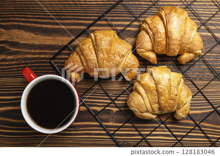 Freshly baked croissants on a cooling tray and a cup of coffee with a wooden background. Top view Freshly baked croissants on a cooling tray and a cup of coffee with a wooden background. Top view 128183046