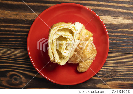 Slices of freshly baked croissants on a red plate with a wooden background. Top view 128183048